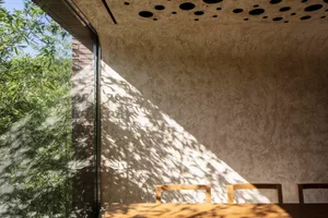 A modern dining room featuring concrete and wood materials with large windows allowing natural light to filter through.