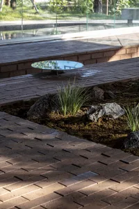 A modern landscape featuring a brick path and circular glass table surrounded by rocks and grass.