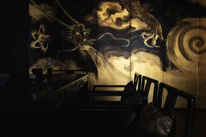 A serene living room with wooden furniture and a black and gold wood panel depicting a Chinese dragon.