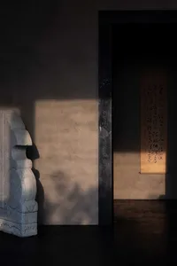A minimalist bedroom decorated with a large concrete sculpture and a framed calligraphy scroll hanging on the wall.
