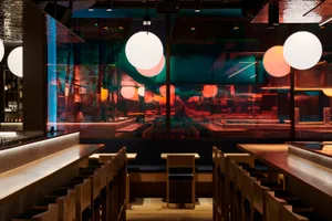 Modern restaurant interior with wooden benches, marble tables, and glass walls.