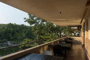 An outdoor seating area in a restaurant with modern design elements, featuring wooden furniture, glass railings, concrete flo