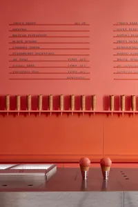 A modern, minimalist food court interior with concrete walls displaying an extensive menu of ice cream flavors and cones.