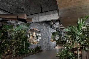 An industrial-style restaurant interior with concrete walls, wooden accents, and lush green plants.