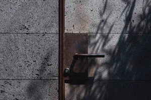 A metal door handle with a shadow cast on a concrete wall.