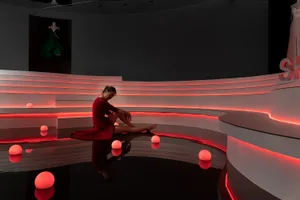 A woman in a red dress sitting on a curved staircase with red lights and reflective surface.