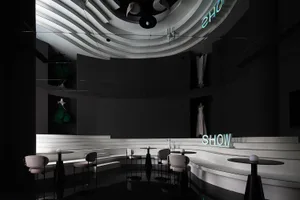 A showroom with concrete platforms, green dresses hanging, and a neon 'SHOW' sign.