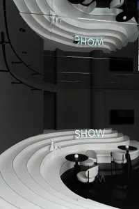 A modern showroom with concrete and white materials, featuring circular seating and a neon sign.