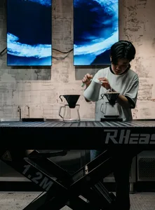 Person preparing coffee in an industrial-themed coffee shop with glassware.