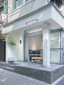 Concrete exterior of a coffee shop with glass doors and a simple seating area inside.