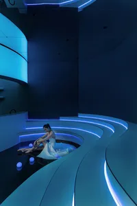 A modern, contemporary photography studio with blue lighting and a woman in a white dress sitting on a curved platform.