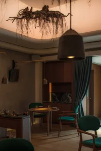 A modern dining room with wooden furniture, green upholstered chairs, and a hanging root chandelier.