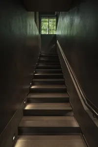 Modern industrial-style staircase with wooden steps, featuring minimalist design and an open area at the top with a view of g