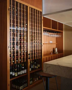 A modern restaurant bar featuring a wooden wine cabinet filled with various bottles of wine and a marble counter.