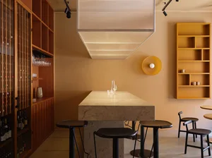 A modern restaurant interior with concrete tables, wooden shelves, and leather stools.