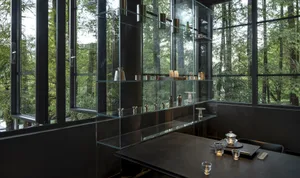 A minimalist restaurant interior with glass walls and wooden accents, featuring sleek metal furniture and a large display cas