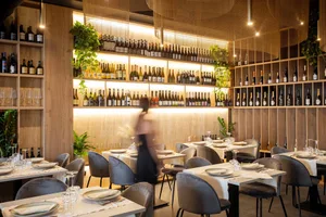 A beautifully designed restaurant interior with wooden walls, glass shelving, metal furniture, and green plants.