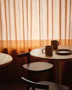 Two wooden tables with brown mugs and plates in a cozy cafe setting.