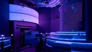 A modern bar club interior illuminated with blue lighting and featuring concrete elements.