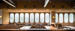 Industrial-style restaurant interior with wooden tables, metal railings, and large oval windows.