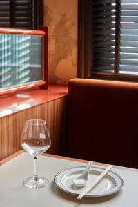 A modern industrial-style restaurant booth with brown wood, a glass wine glass, a plate with chopsticks, and a spoon.