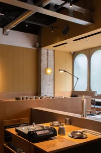 Modern industrial restaurant interior featuring wooden tables, metal stools, and concrete walls with exposed pipes and lighti