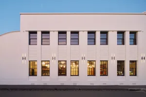 Modern white concrete building facade with a row of windows and illuminated interiors.