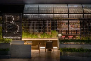Interior view of a modern restaurant and bar with glass walls, concrete seating, and modern decor.