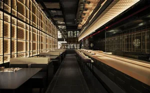 A sophisticated restaurant interior with black walls, wood accents, and a long bar counter.
