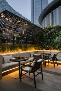 A modern restaurant exterior with concrete and glass materials, featuring outdoor seating area and urban background.