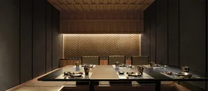 A modern restaurant interior with dark taupe walls and brass accents featuring a long dining table with place settings and me