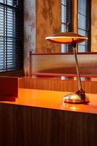 A modern restaurant interior with a metal accent table lamp on a wooden counter, illuminated by natural light through windows