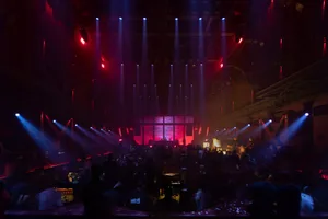 A bustling nightclub interior with a cocktail bar illuminated by colorful lights.