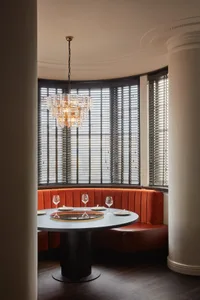 A round dining table with a lazy Susan, glasses, and plates, surrounded by a cozy orange velvet booth seating area with large