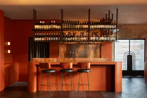 A photograph of a modern restaurant bar featuring red wooden stools and a marble countertop.