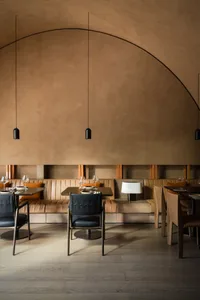 A modern restaurant interior with plush leather seating, wooden dining tables, and sleek black pendant lights.