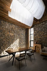 Rustic dining room featuring stone walls, wooden table, and chairs with woven backs.