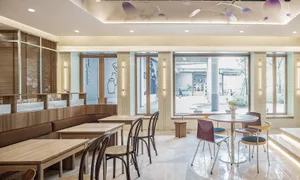 A modern cafe interior featuring wooden tables and chairs, glass partitions, and concrete flooring.