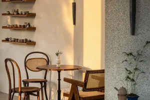 A modern cafe interior featuring minimalist decor, concrete and wooden elements, and ceramic items on a shelf.