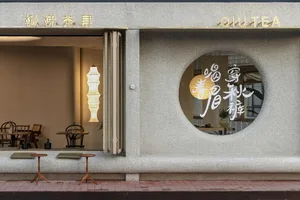 A modern coffee shop exterior with concrete walls, a large round window, and traditional lantern lighting.