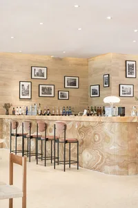 A luxurious restaurant bar with a modern design featuring a marble counter, pink velvet stools, and framed photographs on the