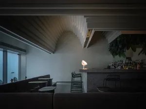 A modern restaurant bar featuring concrete walls and ceilings, with a minimalist design and a cozy, intimate atmosphere.