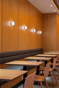 Modern restaurant dining area with wooden tables, chairs, and a wood-paneled wall with recessed lights.