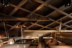 A modern restaurant interior with wooden tables, metal chairs, and concrete floors.