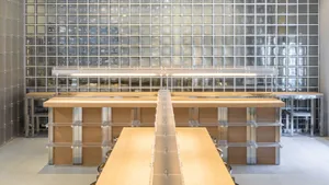 A modern workspace featuring wooden tables, glass walls, and metallic structural elements.