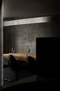 Modern minimalist restaurant interior featuring wooden dining table, concrete accents, and black chairs.