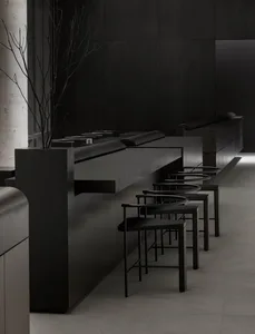 A dark, minimalist restaurant interior with black bar stools, concrete floor, and metallic elements