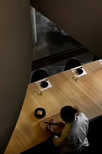 A minimalist restaurant interior with a wooden counter and a chef slicing fish.