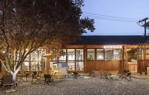 Outdoor cafe with wooden tables and chairs under string lights, featuring a cozy atmosphere with a gravel courtyard and glass
