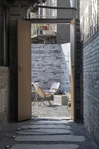 Minimalist architectural space with brick walls and a pathway leading to a seating area with chairs and a table.